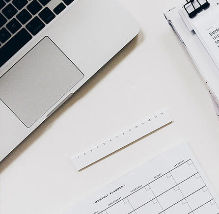 Se puede ver parte de un ordenador, una regla, un cuaderno con cosas apuntadas y un planificador de días